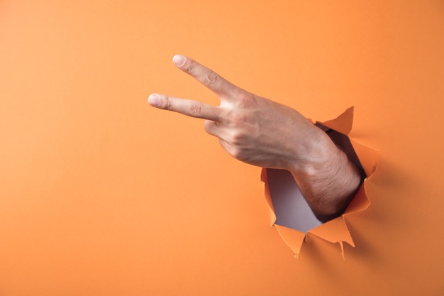 Hand shows peace sign on orange background