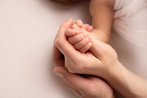 The hand of a sleeping newborn in the hand of mother and father close-up. Tiny fingers of a newborn. The family is holding hands. Studio macro photography. Concepts of family and love.