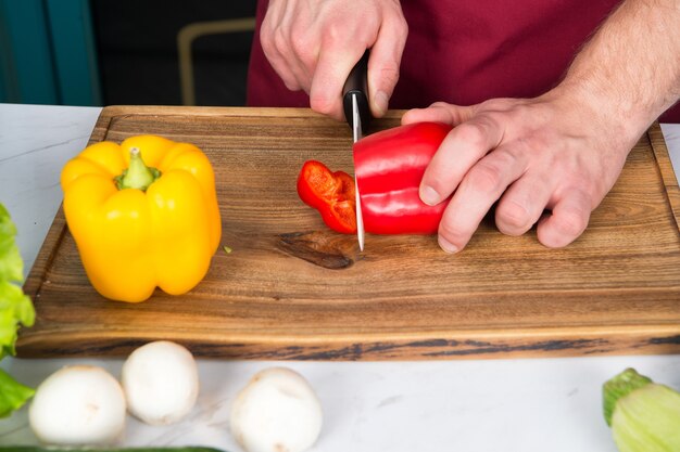 Hand slice pepper with ceramic knife. Vegetables getting cut on wooden cutting board. Food preparation and cooking recipes. Vegetarian menu and healthy diet. Organic products concept.