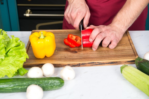 Hand slice pepper with ceramic knife. Vegetables getting cut on wooden cutting board. Food preparation and cooking recipes. Vegetarian menu and healthy diet. Organic products concept.