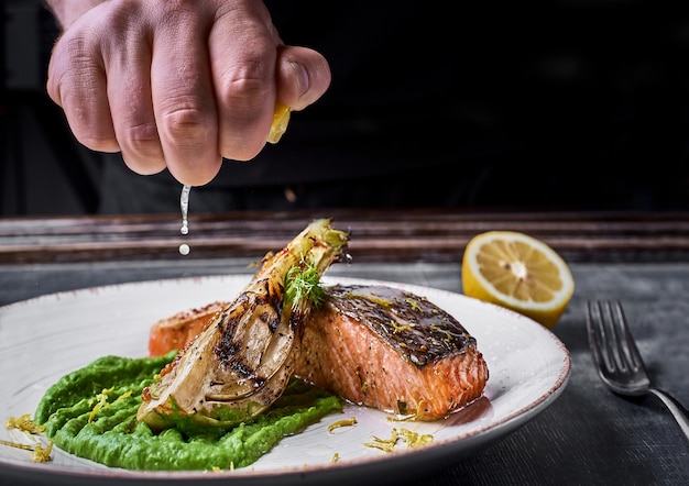 Hand squeezes lemon over Baked salmon steak with mashed green peas , caramelized onions.