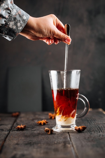 Hand stirring condensed milk in a glass mug with coffee