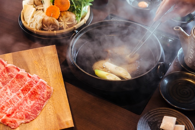 Photo hand stirring hot and boiling shabu broth with  a5 wagyu and kurobuta pork.