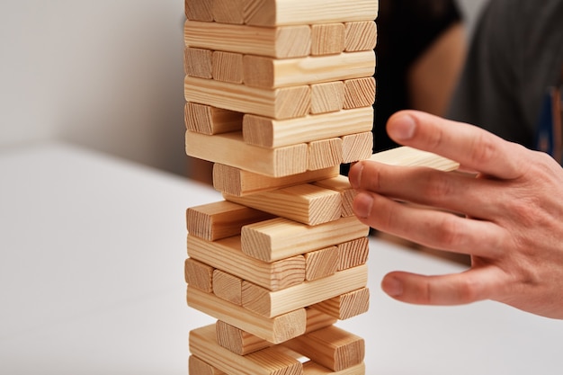 Hand take one block from wooden tower on white background. Family entertainment. Board game