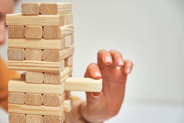 Hand take one block from wooden tower on white background family entertainment board game