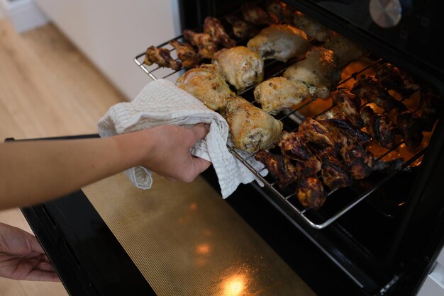 A hand takes out fried chicken wings and legs from the oven