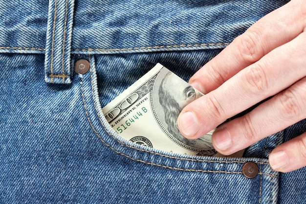 Hand takes or putting in US dollar banknotes in the right front pocket of blue jeans Concept of saving money or pocket expenses