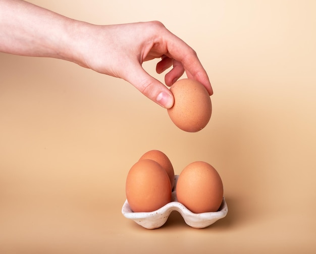 Hand taking healthy chicken egg in eggshell from ceramic holder