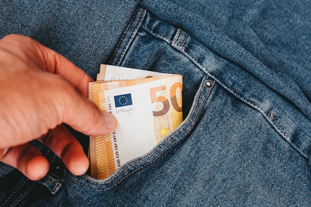 The hand that puts euro banknotes in a pocket of jeans