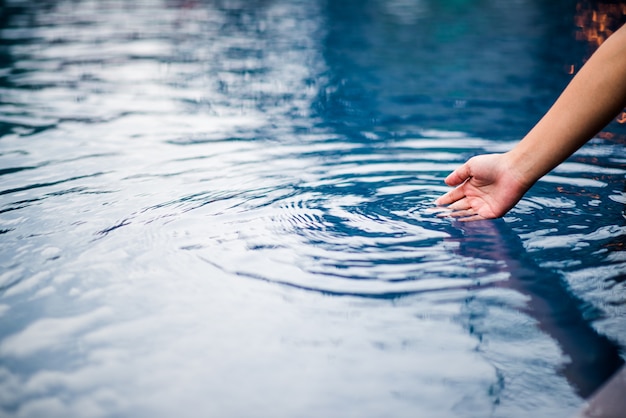 The hand that touches the blue water. The pool is clean and bright. With a drop of water o