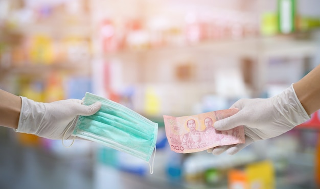 The hand that wears hygiene gloves holds money and holds a mask. Purchase a surgical mask.