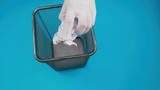 Hand throwing crumpled paper into the office trash isolated on blue background