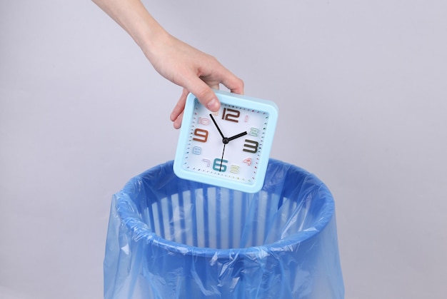 Hand throws alarm clock into trash bin with package on gray background