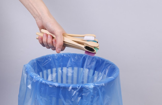 Hand throws bamboo eco toothbrushes into trash bin with package on gray background