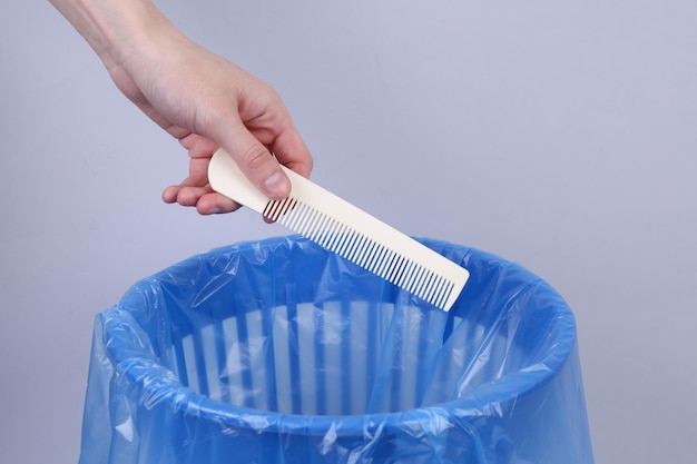 Hand throws plastic comb into trash bin with package on gray background