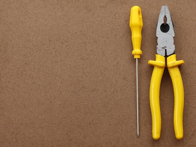 Hand tools for home use pliers and screwdriver on a plywood texture