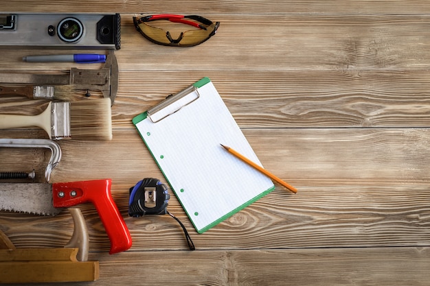 Hand tools on wooden boards. In the center there is a sheet of paper with a pencil.