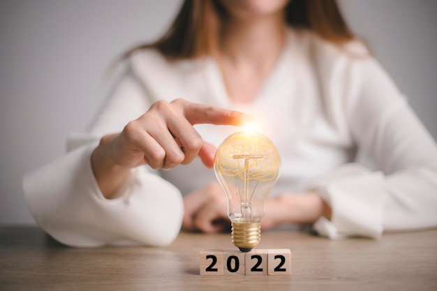 Hand touching on light bulb on wood block with Word 2022, new idea concept with innovation and inspiration,