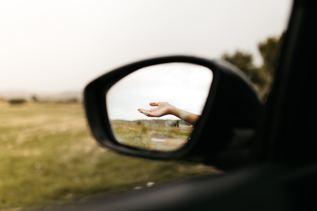 Hand touching rain drops. Mirror seen through the glass. Wet car window. Close up rain drop. Car view see the mirror. Rainy day.