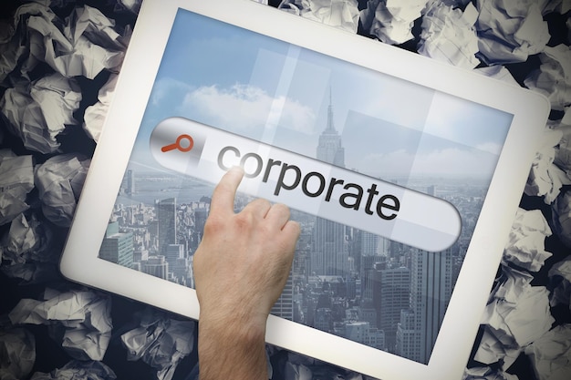 Photo hand touching the word corporate on search bar on tablet screen on crumpled papers