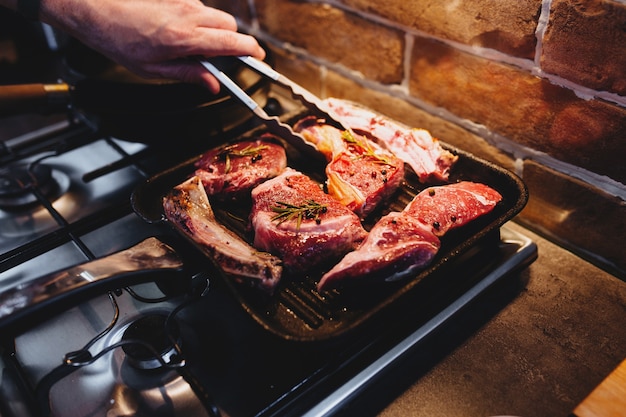 Hand turns steak with tongs during preparation on the grill pan with seasonings