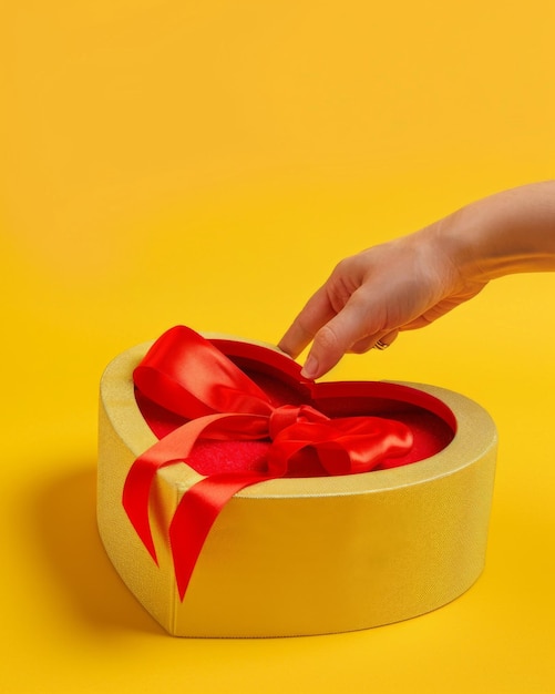 Hand tying bow on red heartshaped box on yellow background for valentines day