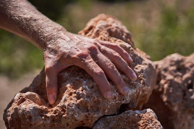 Hand of unrecognizable male tourist leaning on pile of rocks in nature on weekend summer day against blurred background