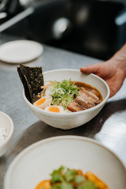 Hand of unrecognizable waiter serving asian noodle soup ramen with meat tofu vegetables nori and egg