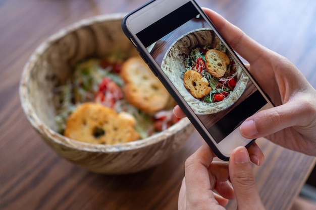 Hand use phone to take photo or take pictures of food. Salad in a bowl placed on the table that looks delicious and tasty. Healthy food for dinner