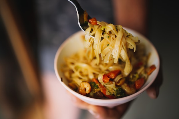 Hand uses fork to pickup tasty noodles with vegetables and shrimp