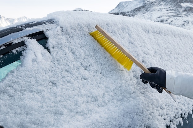 Hand using brush sweeping snow on car windscreen in winter