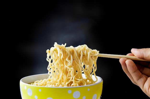 Hand using chopsticks, noodles with steam and smoke in a bowl on black background. Top view, Asian food on the table, food concept