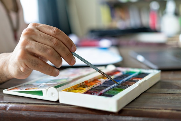 hand using a paintbrush and watercolor palette