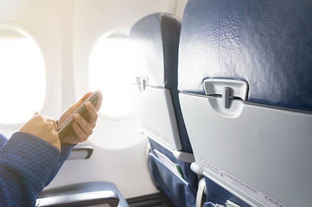 Hand using smartphone and window in airplane with seats in the cabin