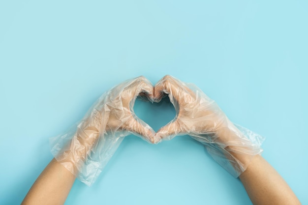 Hand wearing disposable plastic glove making a heart shape isolated on color background