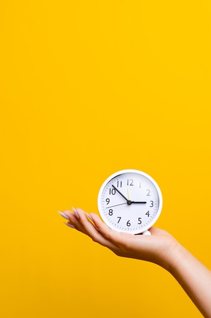 Hand and white alarm clock on a yellow background with space to place text in good work