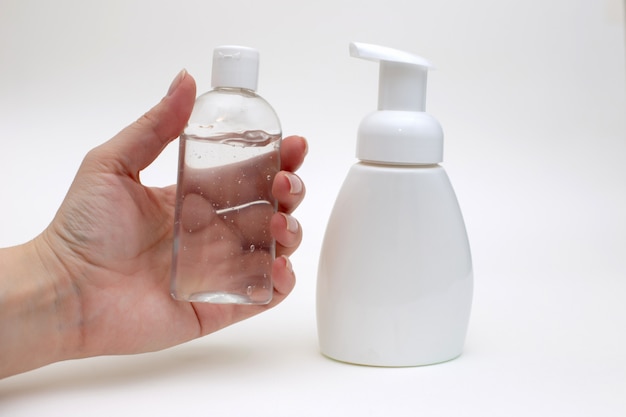 A hand on a white background holds a bottle of antibacterial hand gel sanitizer