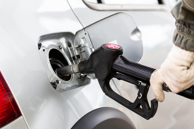 Hand in white cotton fabric glove refueling gray metallic car on gas station closeup with selective focus