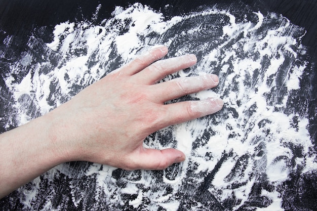 Hand on white flour scattered on black surface.