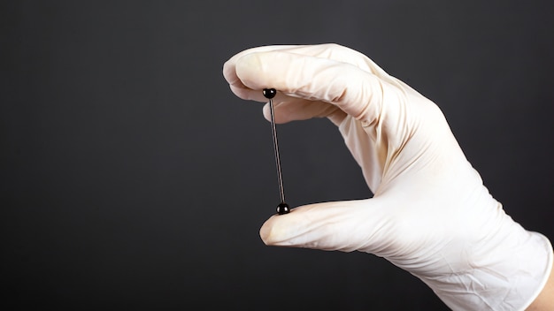 Hand in a white sterile glove holds a piercing for cartilage ear jewelryclose-up.