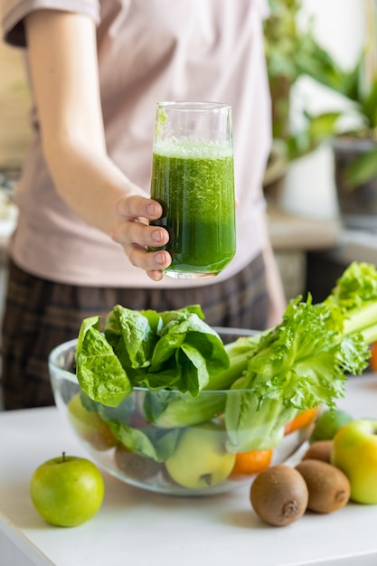 The hand of a white woman in her kitchen makes a green smoothie of fresh fruits and vegetables