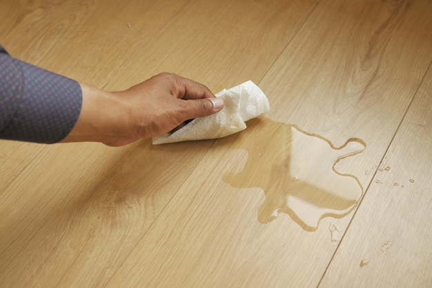 Hand wiping spilled tea with paper napkin on floor