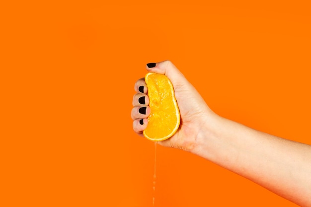 A hand with black nail polish is pouring a quarter of an orange.