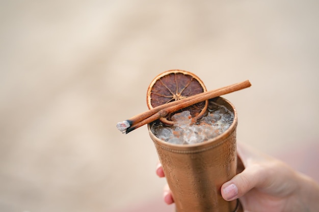 Hand with cocktail, Alcoholic drink with ice, orange and cinnamon on the beach.