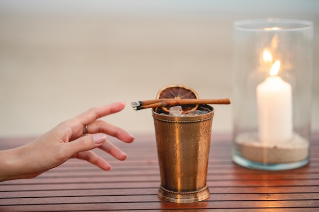 Hand with cocktail, Alcoholic drink with ice, orange and cinnamon on the beach.