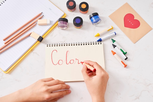 Hand with color pencils and blank sheet of paper on white table