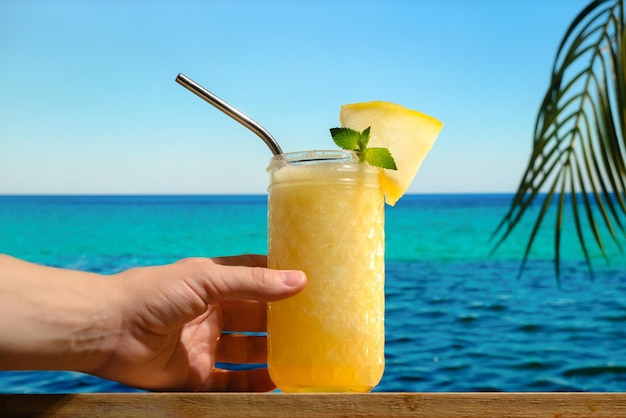 Hand with drinking glass of melon juice on summer beach