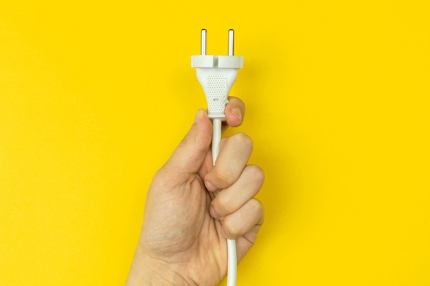 Hand with electrical power cable. Yellow background, flat lay, top view and copy space photo