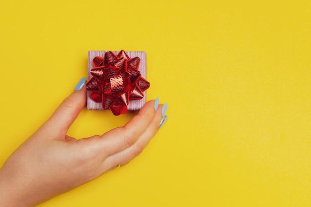 Hand with a gift box on yellow background with free space for text list of presents that you want