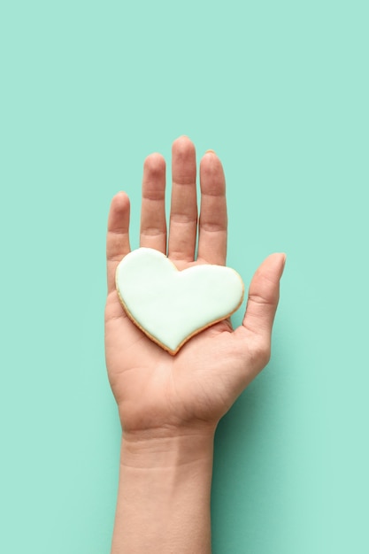 Hand with heart-shaped cookie on turquoise